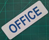 Rectangular White sign with Blue 'OFFICE' text on a green grid background