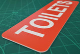 Orange sign with White 'TOILETS' text on a green cutting mat