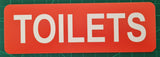 Orange sign with White 'TOILETS' text on a green cutting mat