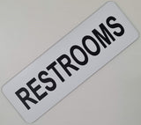Rectangular White sign with Black text  'RESTROOMS'