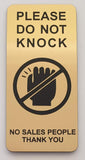 Gold sign on a white wall with Black text 'Please do not knock, no sales people thank you'.