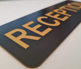 Black acrylic sign with gold letters engraved spelling 'RECEPTION'