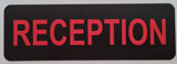 Rectangular acrylic sign with 'RECEPTION' engraved in red on a black background, placed on a white surface.