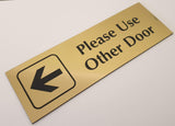 Gold acrylic sign with black engraved text and arrow on a white surface