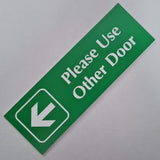 Bright Green acrylic sign with white engraved text and arrow on a gray background