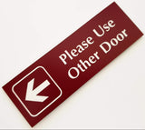 Burgundy acrylic sign with white engraved text and an arrow on a white background