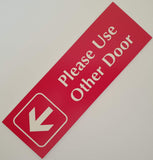 Red acrylic sign with white engraved text and an arrow