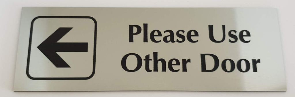 Silver acrylic sign with an arrow and black engraved text 'Please Use Other Door' on a white background