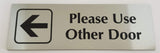 Silver acrylic sign with an arrow and black engraved text 'Please Use Other Door' on a white background