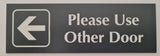 Smoke Grey acrylic Sign with an white engraved arrow and text 'Please Use Other Door' on a plain background