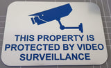 Silver sign with blue text and surveillance camera icon on a gray grid background