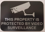 Sign with a camera icon and text 'This property is protected by video surveillance' on a black background.