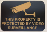 Sign with a security camera icon and text 'This property is protected by video surveillance' on a black background.
