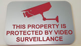 Sign with a red camera icon and text 'This property is protected by video surveillance' on a Silver background.