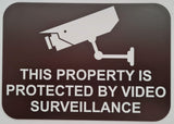Sign with a security camera icon and text 'This property is protected by video surveillance' on a brown background.
