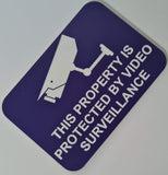 Purple sign with white text and security camera icon on a light gray background