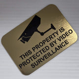 Gold sign with black text and surveillance camera icon on a white background