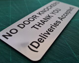 Silver sign with text 'NO DOOR KNOCKERS THANK YOU (Deliveries Accepted)' on a green cutting mat.
