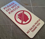 Silver Sign on a door handle requesting not to knock and no salespeople entry.