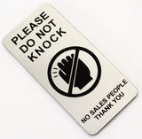 Silver sign with black text and icon stating 'Please Do Not Knock, No Sales People Thank You' on a white background.