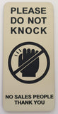 Almond coloured sign with black text and a no-knock symbol on a white background