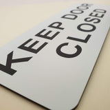White acrylic sign with black text 'KEEP DOOR CLOSED'