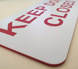 White sign with red text 'KEEP DOOR CLOSED' on a beige surface