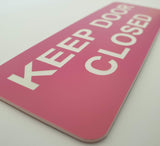 Pink acrylic sign with white text 'KEEP DOOR CLOSED'