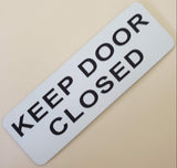 White acrylic sign with black text 'KEEP DOOR CLOSED'