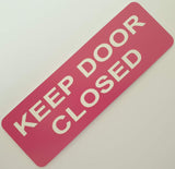 Pink acrylic sign with white text 'KEEP DOOR CLOSED'