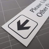 White acrylic sign with black engraved arrow symbol  and text