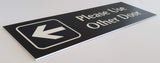 Black acrylic Sign with an white engraved arrow and text 'Please Use Other Door' on a white background