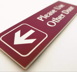 Burgundy acrylic sign with white engraved text and arrow