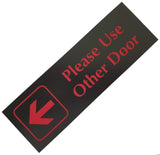 Black acrylic sign with red engraved text and arrow on a white background