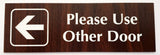 English Walnut acrylic sign with an white engraved  arrow and text 'Please Use Other Door' on a white background