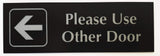 Black acrylic sign with Silver engraved  text and arrow pointing left on a white background