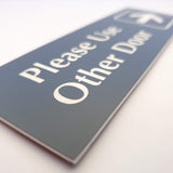 Smoke Grey acrylic Sign with white engraved text 'Please Use Other Door' on a white background