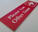 Red acrylic sign with white engraved text and arrow on a white background