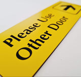 Yellow acrylic sign with black engraved text and an arrow pointing to the right on a white background