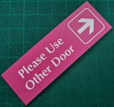 Pink acrylic sign with white engraved text and arrow on a green cutting mat