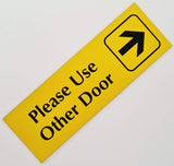 Yellow acrylic sign with black engraved text and arrow symbol on a white background