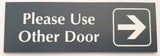 Smoke Grey acrylic Sign with white engraved text 'Please Use Other Door' and an arrow on a white background