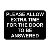 A black square sign with white text that reads 'Please allow extra time for the door to be answered'.