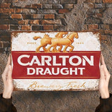 Person holding a Carlton Draught sign against a stone wall background