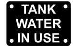 A rectangular black acrylic sign with the words 'TANK WATER IN USE' in white  engraved capital letters, intended for indicating a tank water is in use.